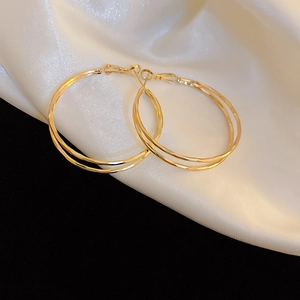 Close-up of golden double hoop earrings on white silk fabric with elegant lighting