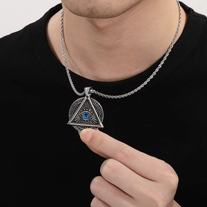 Detail of silver stainless steel triangle pendant with blue evil eye on black shirt