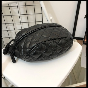 Detail view of a black quilted puffer waist bag with drawstring closure on a chair