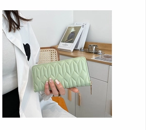 Close-up of mint green quilted long wallet with zipper and diamond pattern held by model