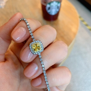 Close-up of a silver bracelet featuring a square yellow gemstone and clear accents on wrist