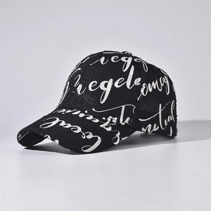 Close-up of black baseball cap featuring all-over white graffiti letter print and curved brim