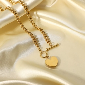 Detailed close-up of golden heart pendant necklace with OT toggle clasp on silk