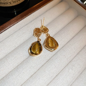 Dettaglio degli orecchini vintage a goccia in occhio di tigre dorato su velluto beige