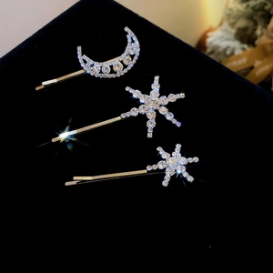 Detail of moon and star rhinestone hair clips on a black velvet background