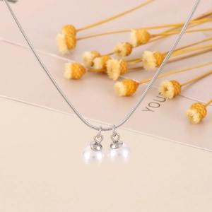 Primo piano di una collana a catena serpente d'argento con due eleganti perle finte bianche