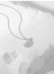 Macro shot of silver ginkgo leaf necklace with pavé zircon stones on white stone