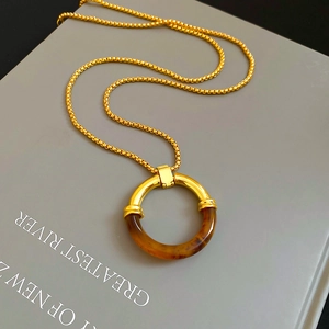 Dettaglio di un ciondolo circolare in resina vintage con catena dorata su un libro