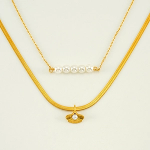 Detail of layered gold ginkgo leaf and pearl necklace set on a beige background