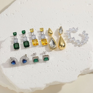 Elegant gold plated drop earrings set with colorful zircon stones on white stone surface