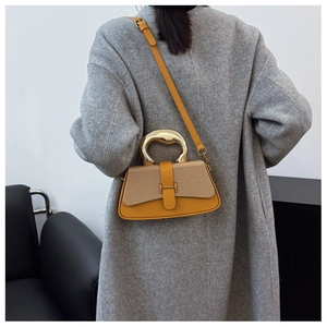 Detail of a mustard yellow and beige box bag with gold H-buckle worn over a grey wool coat