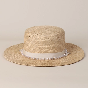 Detail of flat top straw boater hat with wide cream ribbon and faux pearl embellishments