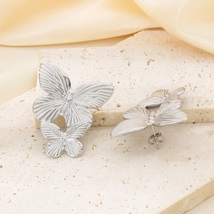 Macro detail of silver butterfly earrings with engraved wings on stone and silk background