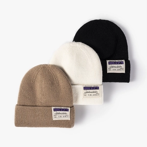 Three ribbed knit beanies in beige, cream, and black with boarding pass label patches