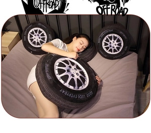 Three 3D car tire plush pillows with Good Luck engraving shown on a cozy bed setup