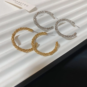 Macro view of gold and silver twisted C-shaped hoop earrings on a white display tray