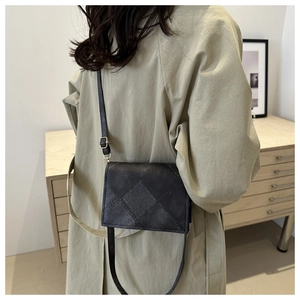 Detail of black quilted leather crossbody bag with thin strap worn over a long trench coat