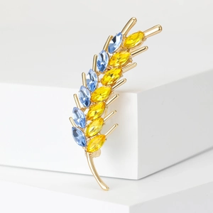 Close-up of golden feather brooch with blue and yellow crystals on white background
