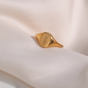 Close-up of golden signet ring with floral lavender engraving on pink silk fabric