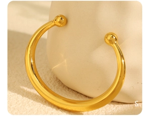 Macro view of golden stainless steel open bangle featuring sphere-shaped ends