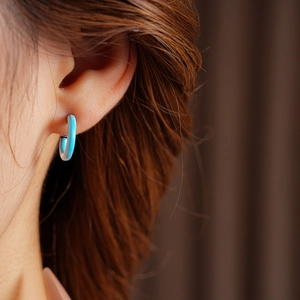 Close-up of model wearing blue enamel C-shaped hoop earrings with a sleek silver finish