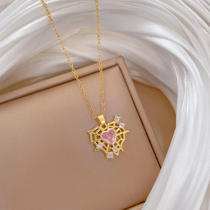 Close-up of gold spider web necklace with pink heart gemstone on beige jewelry box lid