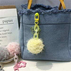 Close-up of yellow plush pom pom keychain with flower charm on blue denim bag