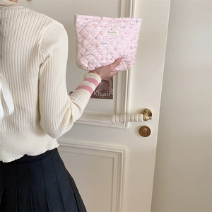 Close-up of pink quilted fabric makeup bag with cute patterns held by a person