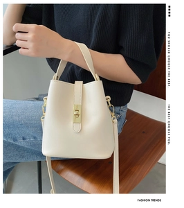 Detail of a chic cream leather bucket bag with gold buckle held by a model