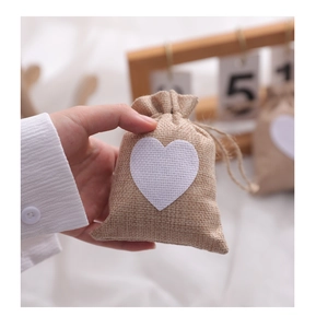 Close-up of small beige burlap drawstring bag with white heart patch for wedding gifts