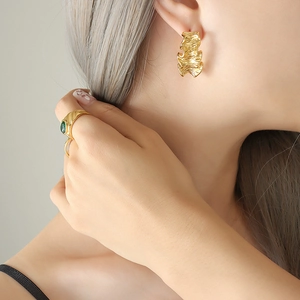 Boucles d'oreilles dorées texturées et bague émeraude portées par un mannequin sur fond sobre