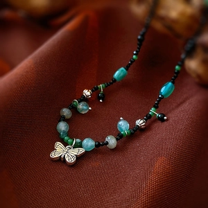 Macro shot of an antique silver butterfly pendant with multi-color stone beads on fabric