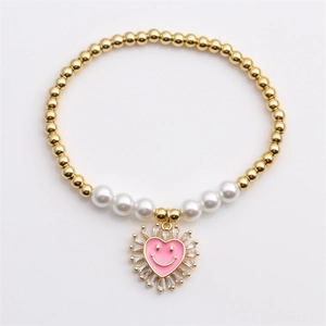 Bracciale elastico dorato con perle e ciondolo a cuore rosa su sfondo grigio pulito