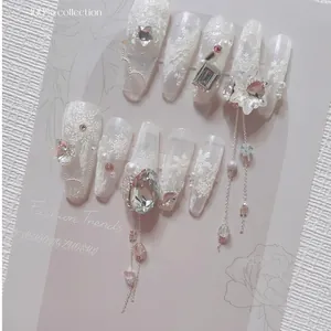 Long oval press-on nails in creamy white with 3D snowflake relief and metal tassels