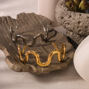 Minimalist 18K gold and silver wavy open bracelets on a stone tray with dry flowers