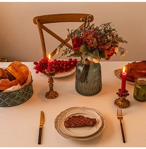 Close-up of elegant gold candle holders and green textured glass vase on lace tablecloth