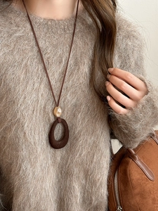 Close-up of a vintage brown resin pendant necklace worn over a soft beige sweater