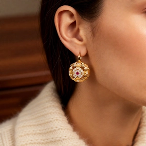 Close-up of vintage gold ball earring with floral filigree and red gemstone inlay