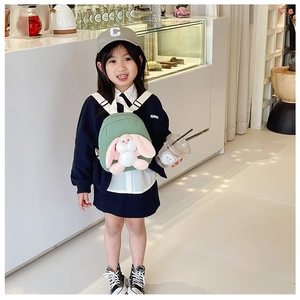 Green kids backpack with long-eared bunny doll shown on child in bright indoor setting