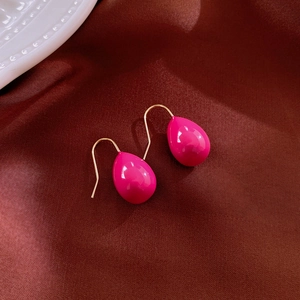Close-up of pink teardrop earrings with gold hooks on a red satin background