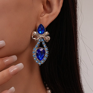 Close-up of teardrop dark blue gem earrings with silver bow and crystal accents