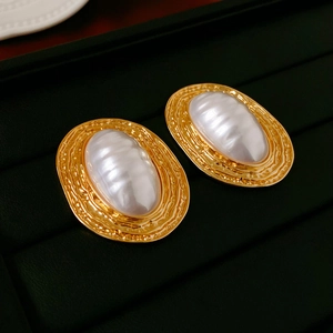 Close-up of vintage oval gold earrings with white pearl inlay and hammer texture