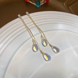 Close-up of golden tassel earrings with iridescent crystal droplets on a white plate