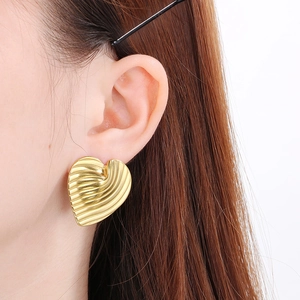 Close-up of golden heart-shaped earrings with textured surface on a model
