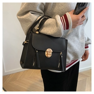 Detail of a black crossbody bag with gold hardware and tassel accents on a model