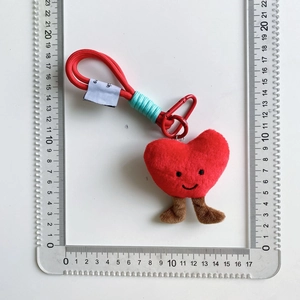 Dettaglio di un portachiavi a cuore di peluche rosso con gambe e clip in metallo su scala