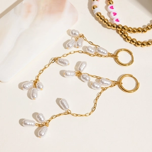 Detail of golden titanium steel hoop earrings featuring cascading white pearl tassels