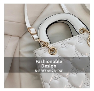 Close-up of white heart-quilted handbag with gold hardware and top handle details