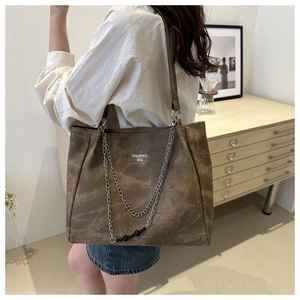 Detail of dark brown tote bag with metal chains on model in a minimalist home setting