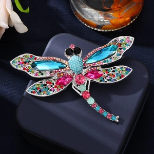 Elegant silver dragonfly brooch with colorful rhinestones on a navy jewelry box